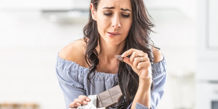 guilty expression of a woman who bites off from a chocolate bar