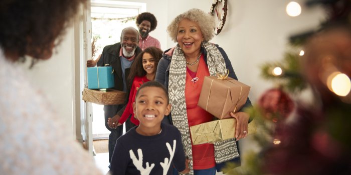 grandparents being greeted by family as they arrive for visit on christmas day with gifts