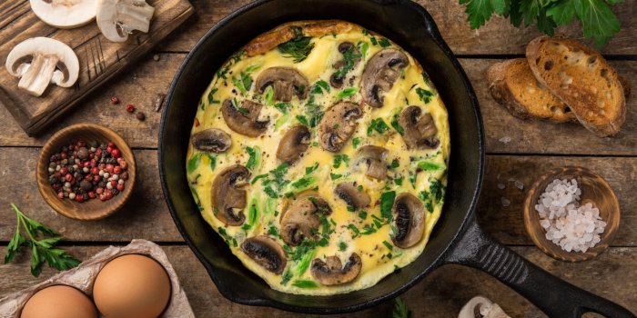 omelette with mushrooms on cast iron pan, top view, wooden background