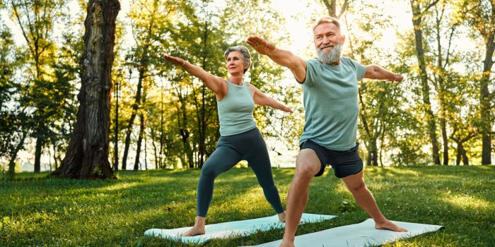 determined family couple standing on rubber mats in national park and performing warrior asana pose aged man and woman sh...