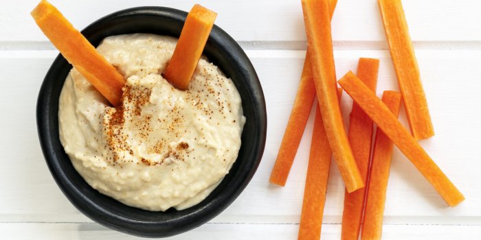 hummus with carrot sticks top view over white timber