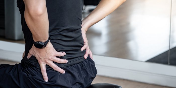 sport man feeling lower back pain or spine pain while sitting on workout bench in fitness gym male athlete suffering from...