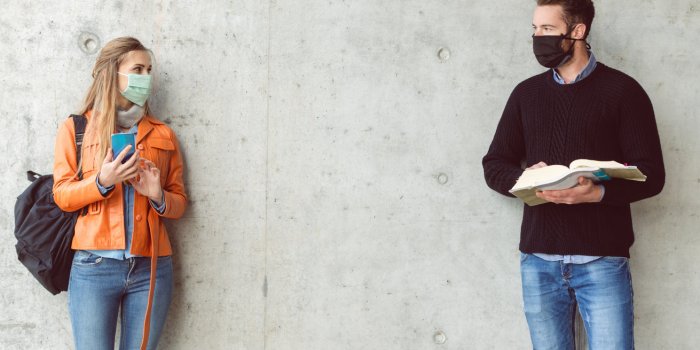 two students standing in social distance wearing face mask looking at each other