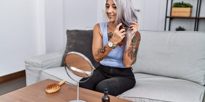 middle age grey-haired woman having hair treatment sitting on sofa at home