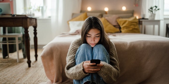teenage girl sitting on the floor and scrolling her smartphone