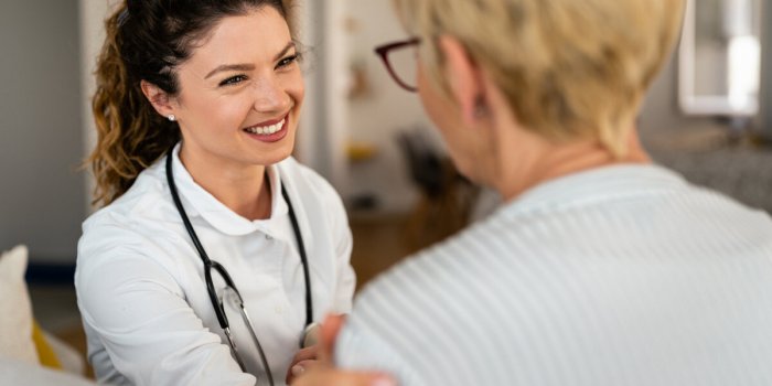 happy smiling female doctor at home visit talking to unrecognizable senior blonde woman support, trust and empathy during...
