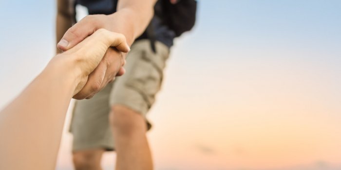 hiker giving his hand helping partner climb up to the top of mountain
