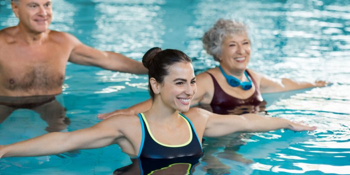 smiling fitness class doing aqua aerobics in swimming pool smiling young woman with senior couple stretching arms in swim...