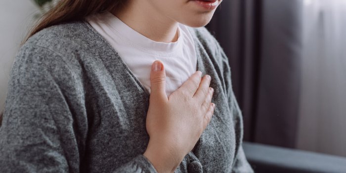 close up of ill sad young caucasian woman putting hand on chest, feels discomfort having pain in chest, gastroesophageal ...
