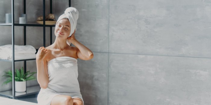 relaxed young caucasian female model wears towel wrapped on head, feels refreshed after taking shower, has healthy clean ...