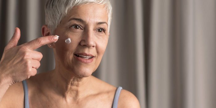 beautiful mature woman with short gray hair putting some cream on her face, skin care concept
