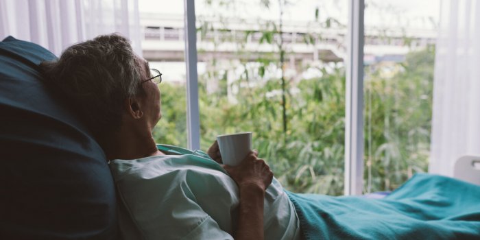 senior man on a hospital bed alone in a room looking through the hospital window elderly patient