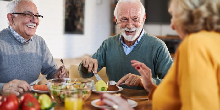 group of happy senior friends talking while having a meal at dining table