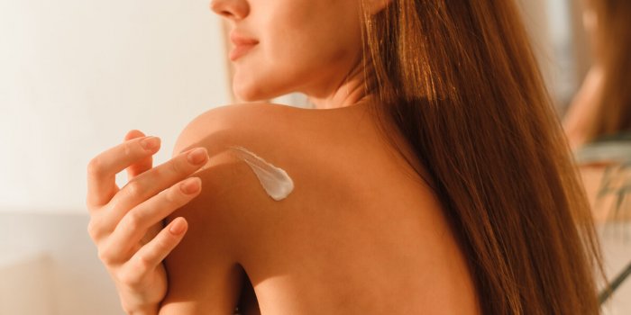 a young woman puts cream on her body in the bathroom moisturizing the skin after a shower