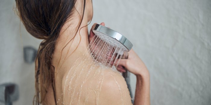 back view of a caucasian female with loose long blonde hair standing under the jet of water