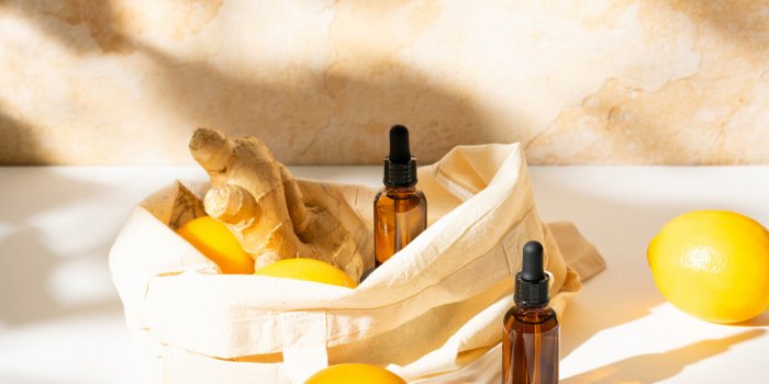 sunlit scene of brown glass cosmetic serum bottles with lemon and ginger in a cotton canvas tote bag on bright earthy bac...