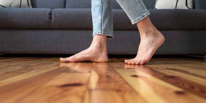 cropped shot of female legs walk barefoot on wooden warm floor near couch in living room at home, heating concept