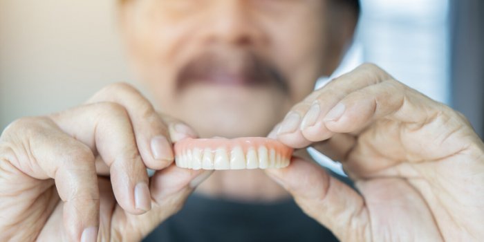 grey haired senior man holding orthodontic prosthesis denture with a happy face standing and smiling with a confident sel...