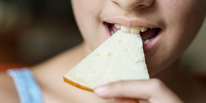 closeup of unrecognizable teenage girl eating delicious cheese slice at home
