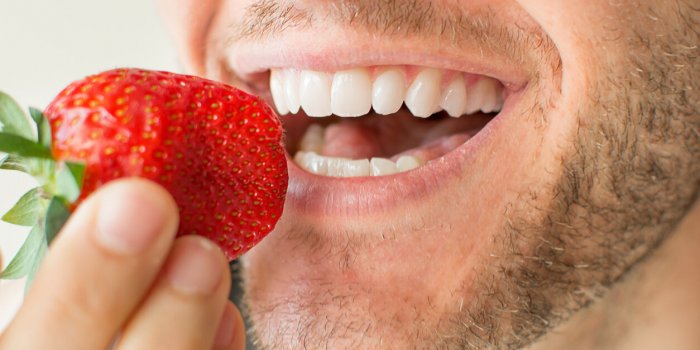 closeup of a man's face eating fruit with big smile