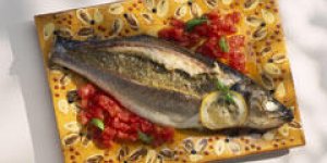 Loup farci aux olives, tomates confites et pignons
